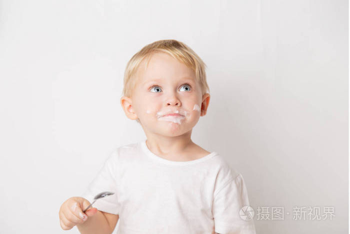 一个金发碧眼的白人小男孩在白色背景上用勺子吃酸奶