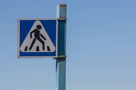 Road sign pedestrian, on an iron pole, against the blue sky.