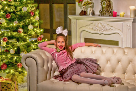 漂亮的小女孩坐在圣诞树旁的沙发上。