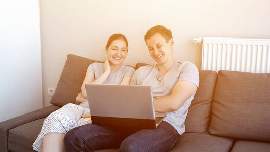 男人和女人坐在沙发上笑着用笔记本电脑看喜剧电影。