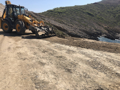 黄色装载机反铲正在规划道路施工期间的路面。土方挖掘挖掘