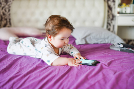 儿童和移动设备。小女孩躺在床上看着智能手机