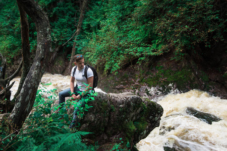 背着背包坐在森林里岩石上的男旅行者。