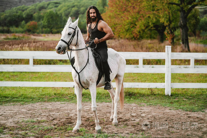 骑着灰色阿拉伯马在田野里一个英俊的大胡子男人在农