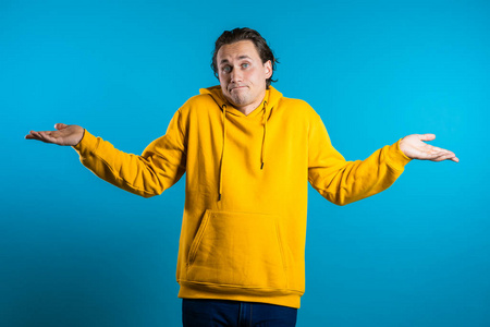 年轻帅气不确定的家伙穿着黄色连帽衫耸了耸肩,做了一个我不知道的