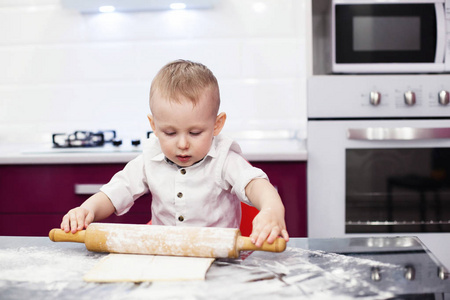 正在准备面团的小男孩。男孩在厨房里揉面团。孩子把披萨面团擀出来。