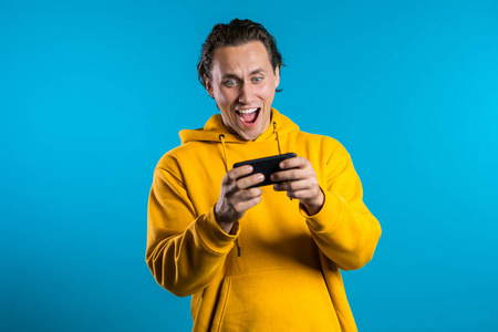 在蓝色工作室墙上的智能手机上玩游戏的帅哥。使用现代技术应用程序社交网络。