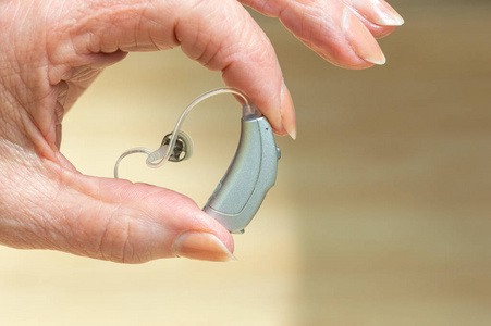 耳朵后面的助听器夹在退休人员的手指之间。
