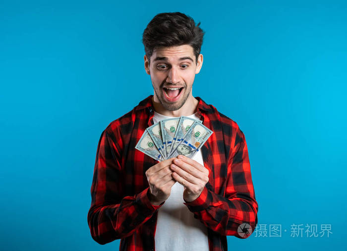 一个穿着红色格子衬衫的男人手里拿着美元,脸上露出惊讶的快乐表情.