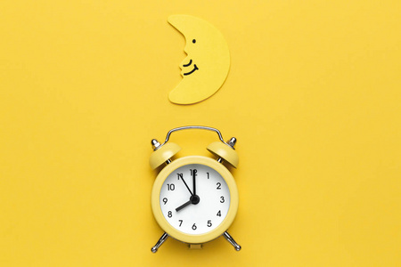 黄色的闹钟和黄色背景上的月亮.照片