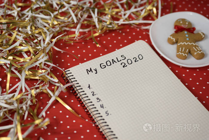 把2020年的目标记在笔记本上。红色背景的姜饼。新年概念