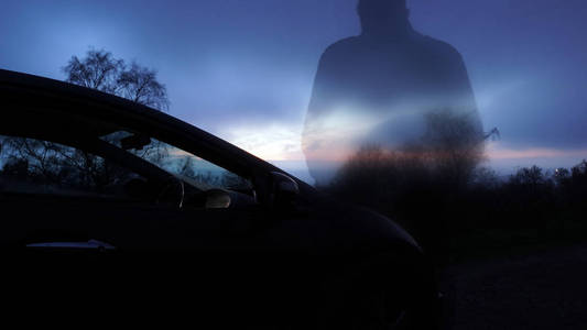 一个幽灵般透明的男人背对着摄像机，站在一辆车旁，在冬天的傍晚眺望日落。有毛刺，离焦，景深效应。