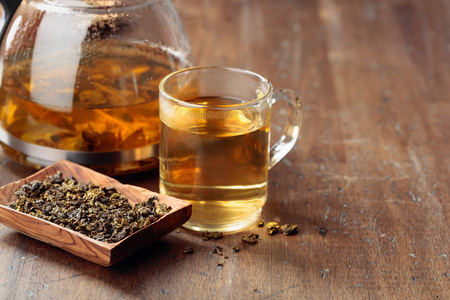 Hot green tea in glass mug. Dried tea leaves and hot drink on a 