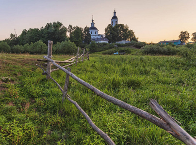 Country orthodox church on sunset in front of green meadow 