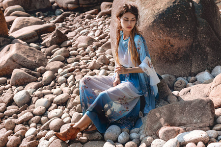 beautiful young woman in elegant stylish dress on stone beach 