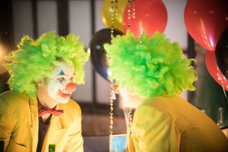 小丑概念-一个迷失的人小丑穿着黄色夹克和绿色假发看着自己照片