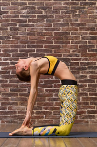 Beautiful woman with slender body doing yoga in on a brick wall 