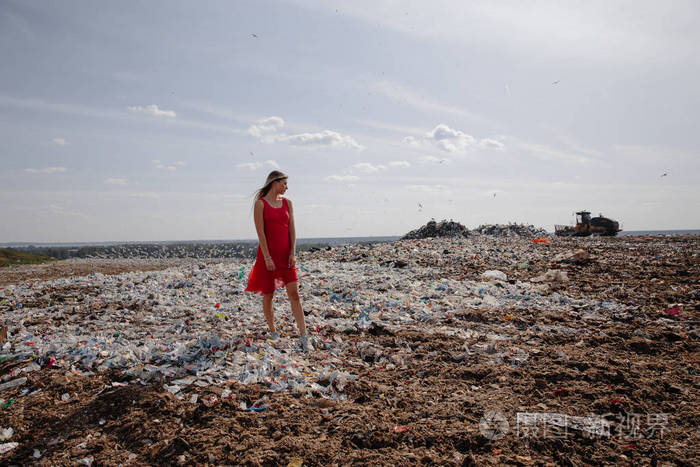 自然污染活动家在一个巨大的垃圾场户外年轻的金发女人穿着红色裙子看着我们世界上所有的人类垃圾和塑料海鸥在东欧拉脱维亚里加飞行