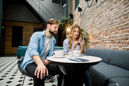 一对年轻夫妇坐在咖啡厅或酒店咖啡厅的桌子旁，用智能手机观看媒体内容