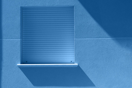 极简的蓝色窗户,墙上有太阳的影子.挂在房子侧墙上的蓝色方形窗户照片