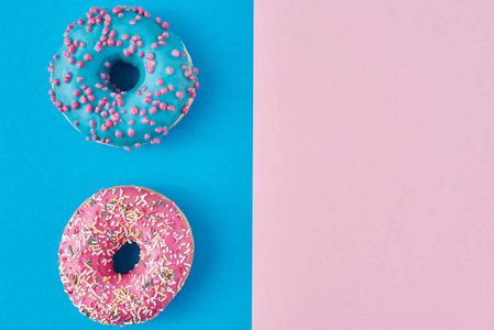 两个甜甜圈在淡粉色和蓝色的背景上。极简创意食物构成。平铺式