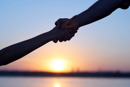 女性援助伸出援助之手.剪影两只手,男人和女人,紧握在天空夕阳下照片