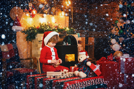 可爱的宝贝，圣诞快乐。圣诞属性。圣诞老人小帮手。圣诞快乐。微笑的小男孩戴着圣诞老人的帽子在家里的圣诞树上。