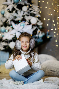 圣诞树旁拿着礼品盒的小女孩