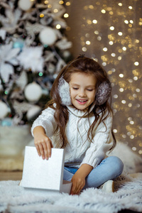 圣诞树旁拿着礼品盒的小女孩
