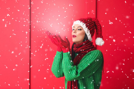 美丽的年轻女子戴着圣诞帽在彩色背景上玩雪