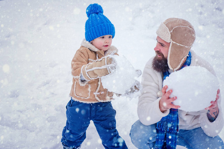 冬季雪装饰。幸福的家庭和雪人一起在雪地里散步。父子俩在冬日的白色背景上打雪仗。