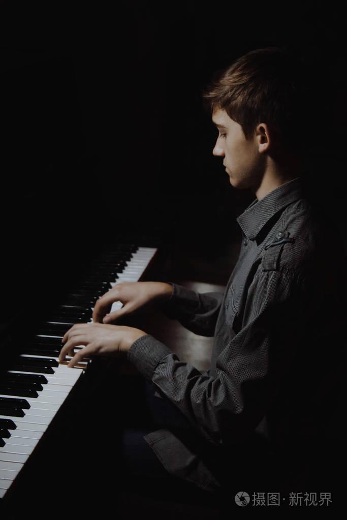 坐在钢琴前的年轻人在音乐学校里男孩情绪化地弹奏键盘乐器学生学会玩