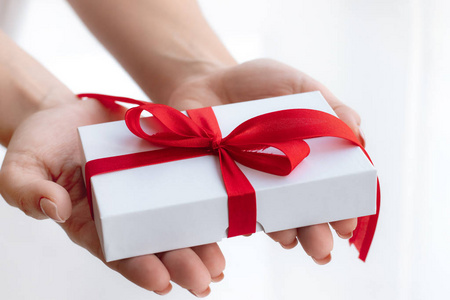 礼品盒，红色丝带蝴蝶结隔离在明亮的白色背景上。把情人节的礼物传来传去。爱和假日的概念。