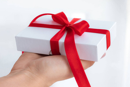 礼品盒，红色丝带蝴蝶结隔离在明亮的白色背景上。把情人节的礼物传来传去。爱和假日的概念。