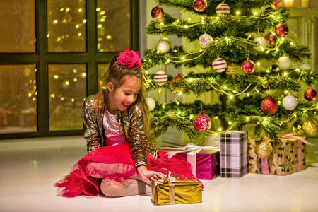 可爱的小女孩拿着礼物在圣诞树旁微笑