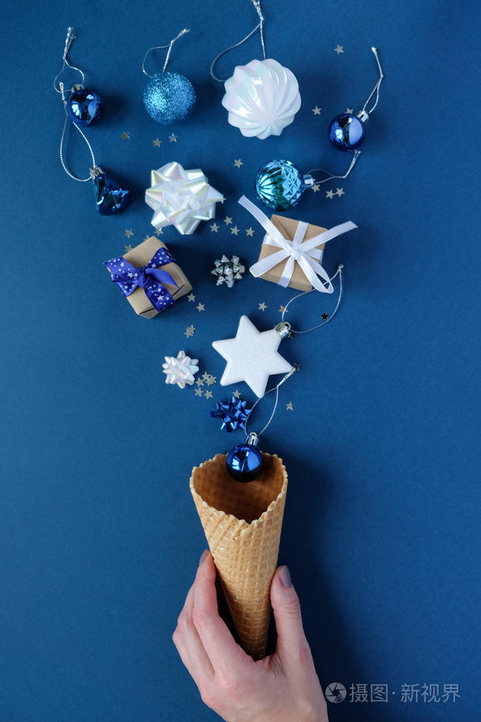 手拿着一个华夫饼圆锥体蓝色背景上有圣诞元素假日概念