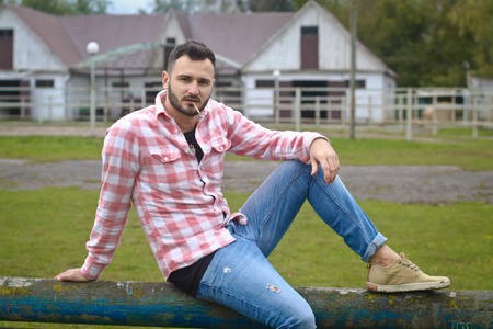 肌肉帅哥马眼年轻帅哥牛仔.一个男农夫正坐在农场的篱笆上.乡村景观.