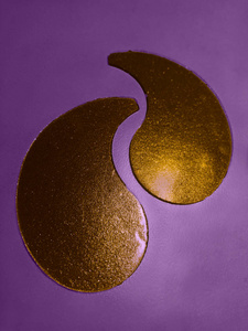 紫罗兰色背景的金色胶原蛋白眼罩。