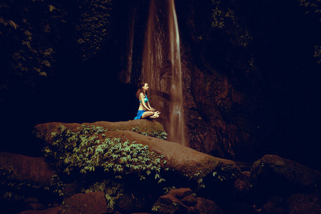 Young Caucasian woman meditating, practicing yoga at waterfall. 