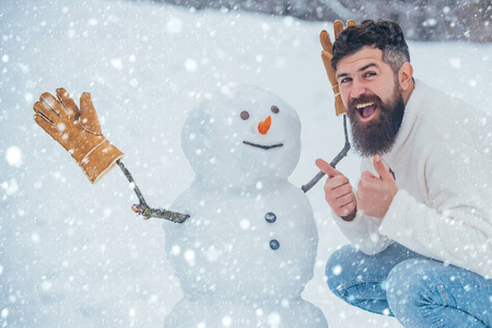 雪地里的圣诞老人。享受大自然的冬日时光。英俊的胡子男人，穿着冬装的父亲。白雪背景上的圣诞老人和雪人。
