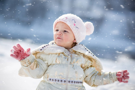 穿着白夹克的小女孩玩得很开心，在外面玩，被雪包围着。