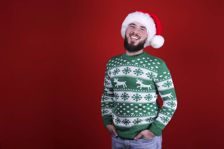 一个年轻人，胡子梳得整整齐齐，穿着圣诞装，背景是红墙。