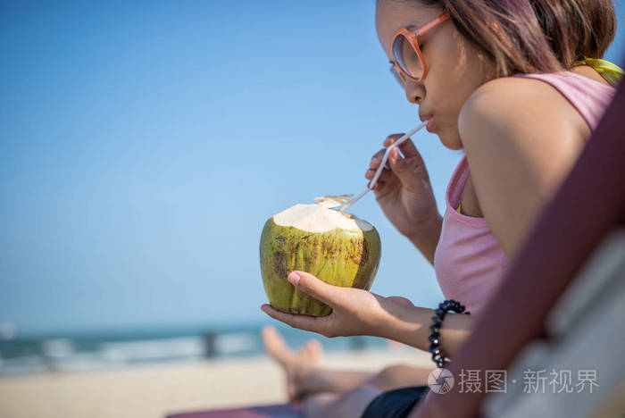 亚洲妇女在美丽的热带海滩喝新鲜椰子汁