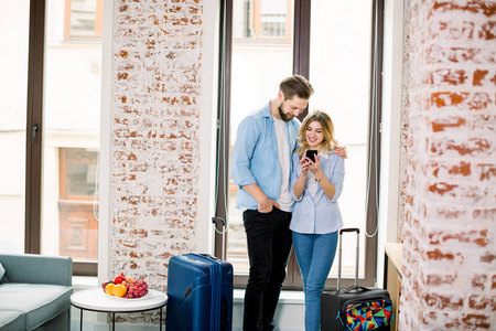 一对幸福的夫妇站在一个现代化的砖墙旅馆的窗户背景上，用智能手机寻找照片