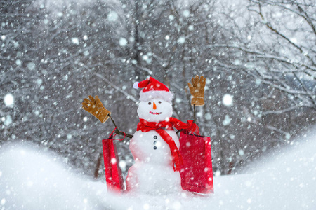 圣诞雪人，带购物袋和圣诞礼物。节日艺术贺卡。新年横幅。雪地上戴着帽子和围巾的可爱雪人，带着惊喜的圣诞礼物。