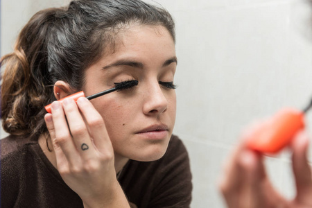 年轻女子在浴室的镜子前涂睫毛膏。