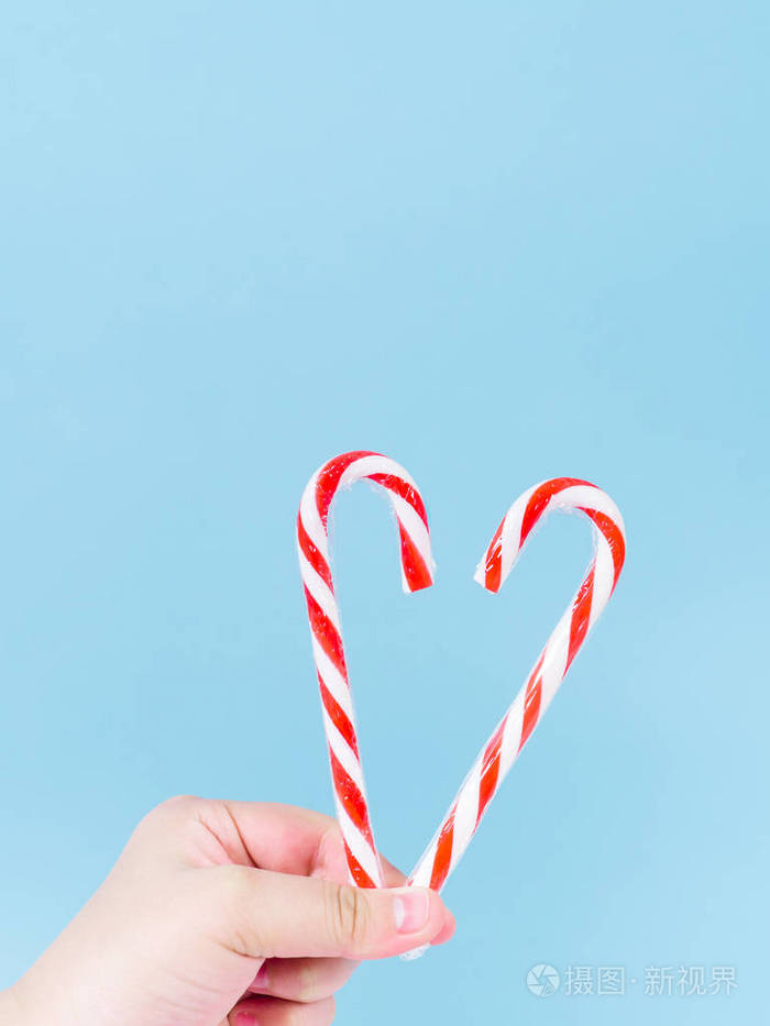 蓝色背景上手捧心形圣诞糖果棒