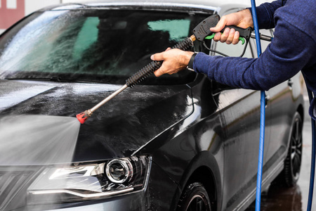 一个男人正在自助洗车店洗车.高压车辆清洗机用水清洗.洗车设备照片