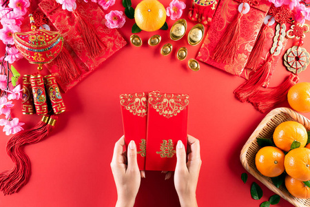 中国新年装饰品。女人手拿战俘或红包，红色背景上有橙色和金色的锭。汉字福的意思是好运好运财富金钱流动。