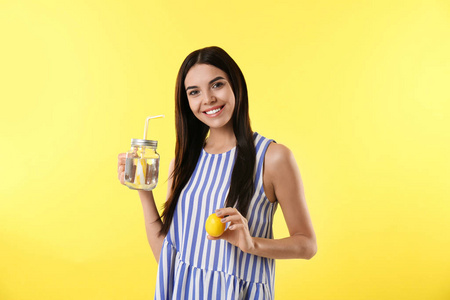 Beautiful young woman with tasty lemon water and fresh fruit on 